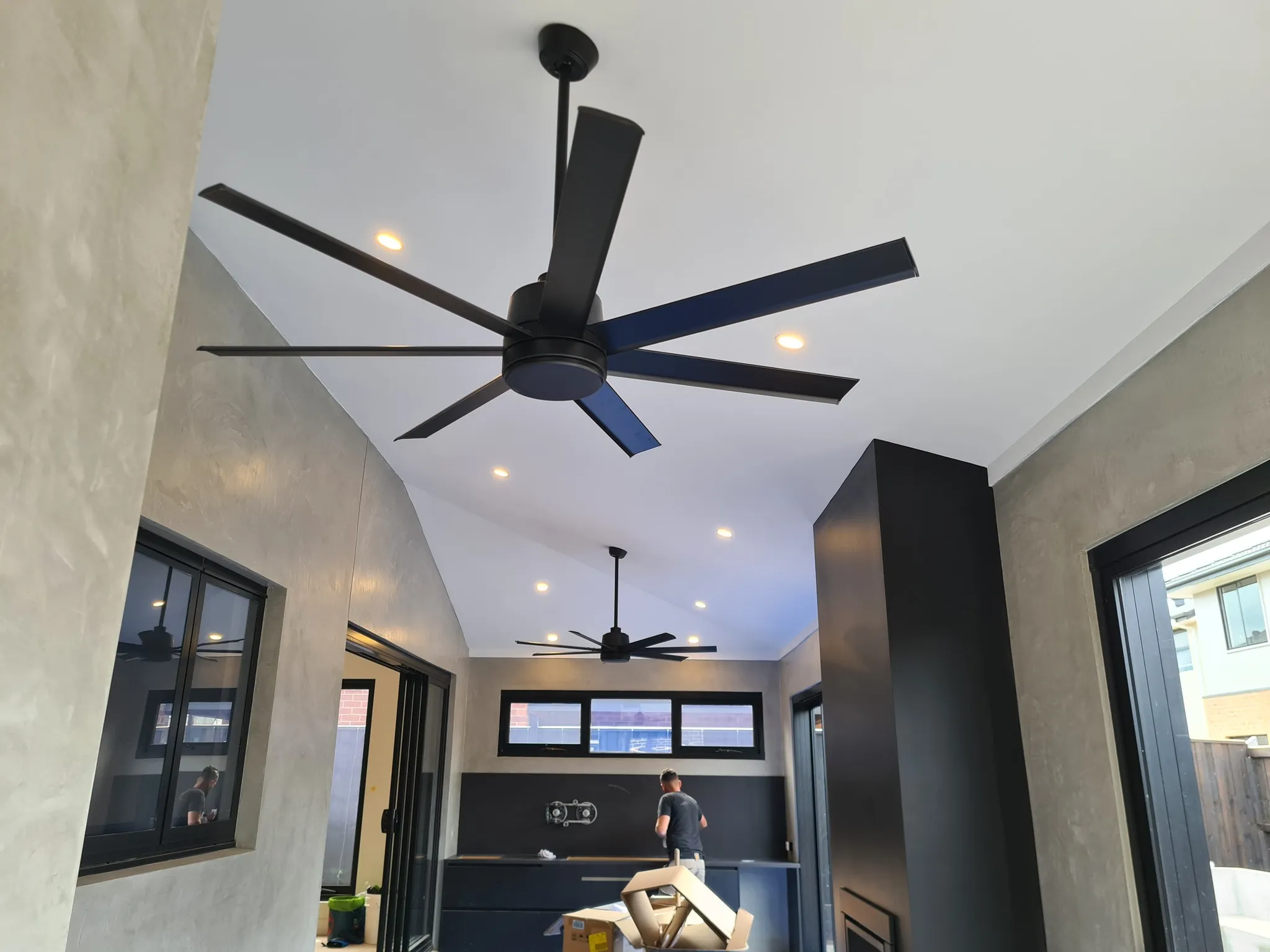 Large black ceiling fans installed in a modern open-plan home with a vaulted ceiling
