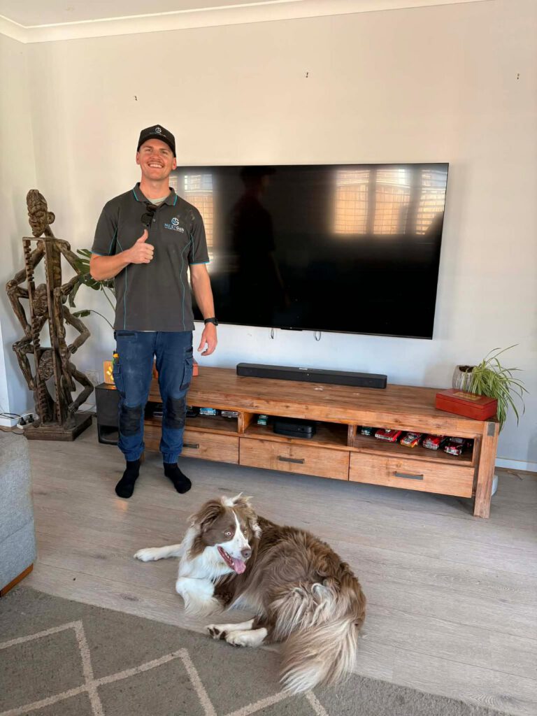 Harley in front of a wall-mounted TV and soundbar he installed, with the client's border collie
