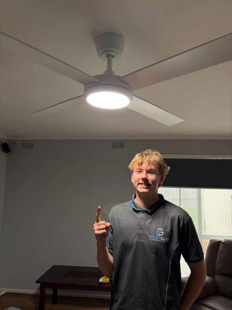 Jakob pointing up at a newly installed white ceiling fan with integrated LED light in a Bacchus Marsh living room