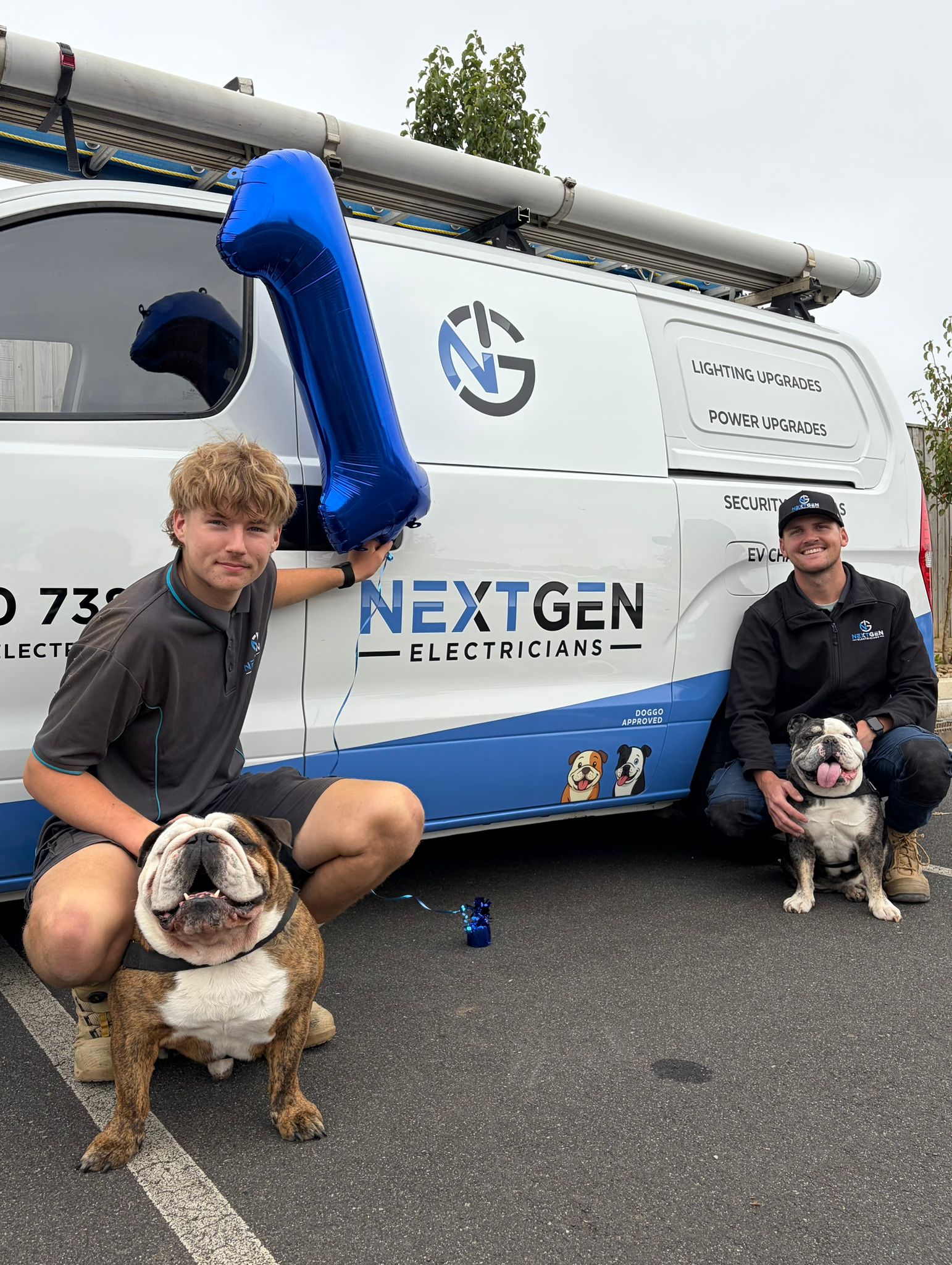 Jakob and Harley from NextGen Electricians crouched with their two British bulldogs in front of the work van