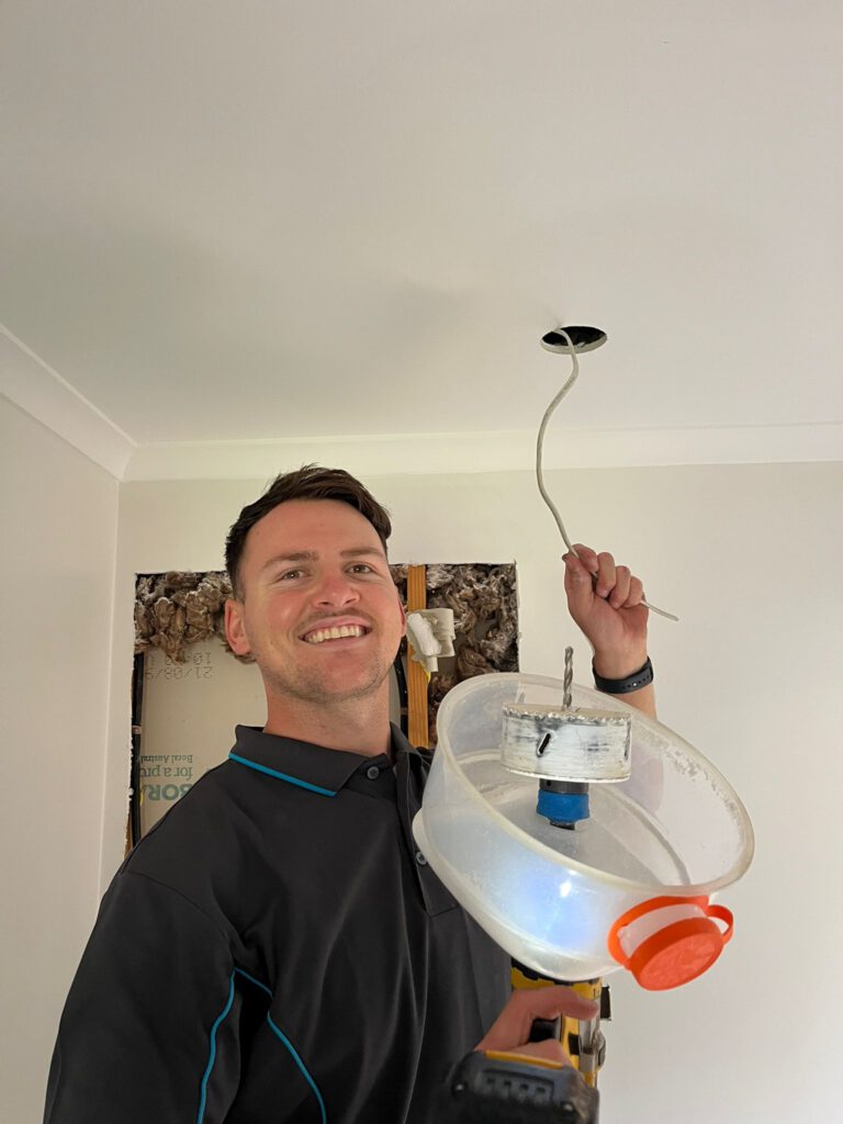 Harley using a downlight hole saw to cut a new ceiling opening during a downlight install