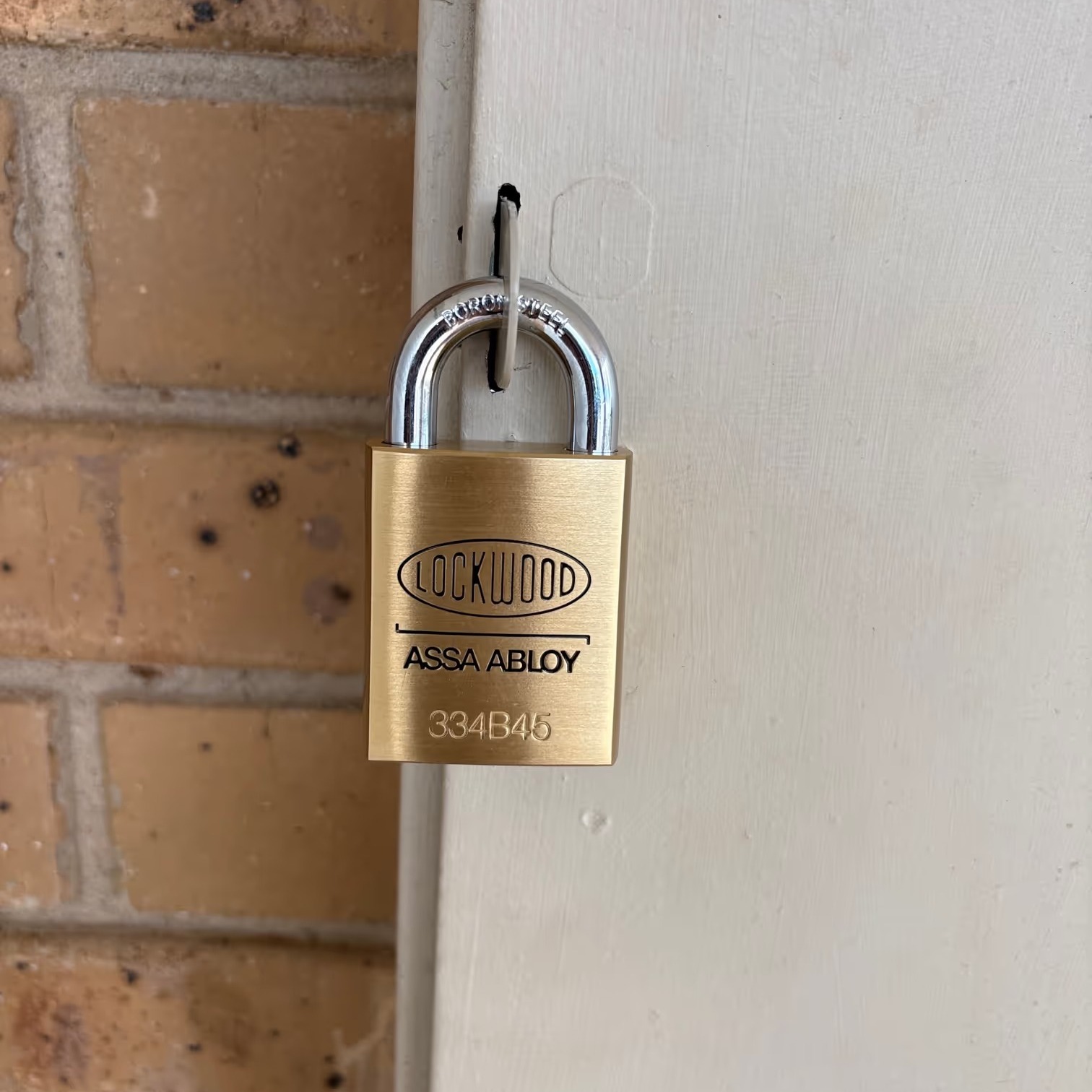 Lockwood Assa Abloy brass power industry padlock installed on the side of an exterior meter box on a brick wall