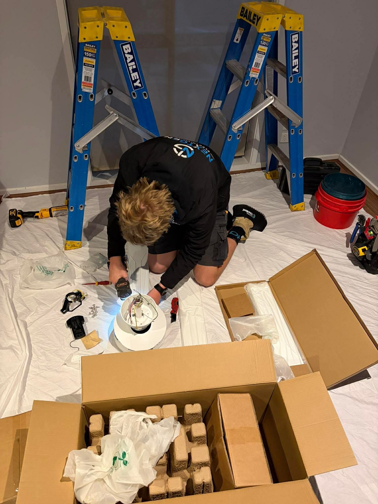 NextGen electrician on a drop sheet assembling and installing a new light fitting during an on-site job
