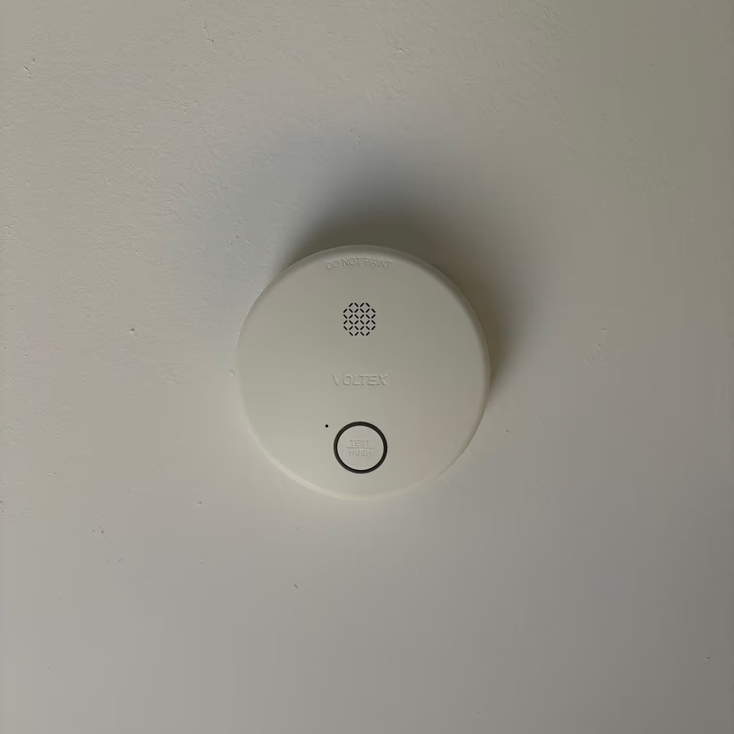 Close-up of a Voltex photoelectric smoke alarm with test and hush button installed on a ceiling